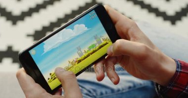 New York - 01 Aralık 2017: Yakın, kızgın kuşlar uygulama siyah akıllı telefon üzerinde yatay olarak oynayan eller mans. Patterened halı ve arka plan üzerinde. Üstten Görünüm
