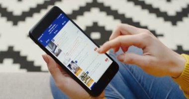 New York - 01 Aralık 2017: Dikey siyah akıllı telefondaki Booking.com uygulamasını kullanarak Kafkas kadınlarının ellerini kapatın. Bulanık arkaplanda desenli halı.