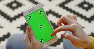 Beyaz smartphone ile yeşil ekran dikey olarak tutan eller ve kaydırma ve üzerinde kaydediyor. Desenli kat arka plan bulanık. Omuz üzerinden. Chroma anahtar. Hareket izleme