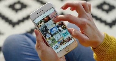 New York - 01 Aralık 2017: Instagram app beyaz Smartphone fotoğraflarda kaydırma eller en iyi görünümü. Desenli kat arka plan bulanık. Yakın çekim