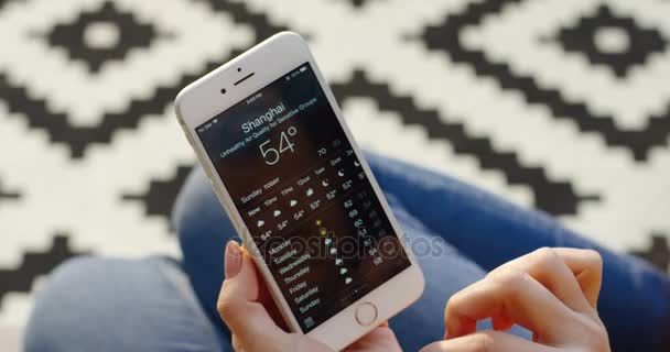 New York - 01 Dec, 2017: Ovanifrån av kvinnans händer rullning på väderprognosen på vita smartphone. Mönstrad matta suddig bakgrund. Närbild — Stockvideo