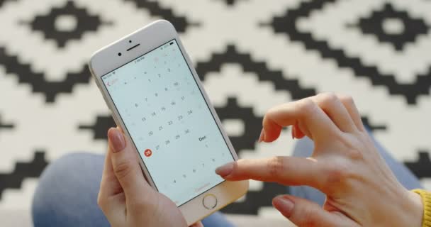 Nueva York - 01 de diciembre 2017: Vista superior de las manos de las mujeres desplazándose en la aplicación de calendario en el teléfono inteligente blanco verticalmente. Alfombra estampada fondo borroso. De cerca. — Vídeos de Stock