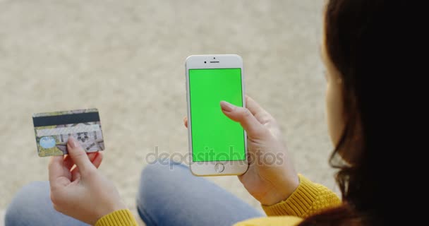 Primer plano de las manos de las mujeres que sostienen el teléfono inteligente blanco con pantalla verde verticalmente y tarjeta de crédito mientras hacen compras en línea. Sobre el hombro. Clave de croma . — Vídeo de stock
