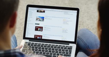 New York - 01 Aralık 2017: omuz görünümü üzerinde Amazon Web sitesinde dizlerine yalan dizüstü bilgisayar üzerinde kaydırma çift üzerinde. Yakın çekim. Üstten Görünüm