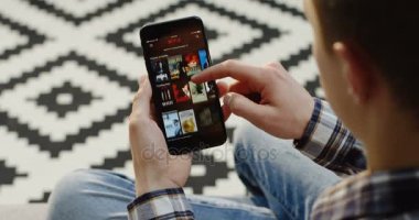 New York - 01 Aralık 2017: omuz görünümü üzerinde siyah Smartphone'da izlemek için bir şey seçmek için Netflix app kullanarak beyaz adam. Yakın çekim. Üstten Görünüm