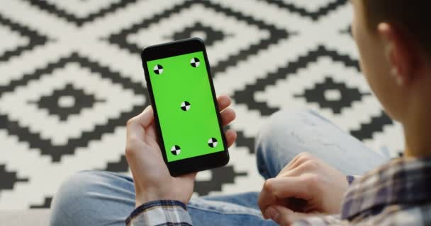 Smartphone negro con pantalla verde y movimiento de seguimiento en manos del hombre caucásico. Verticalmente. Dedos desplazándose, acercándolo y grabándolo. Fondo de piso borroso con dibujos. De cerca. Clave de croma . — Vídeos de Stock