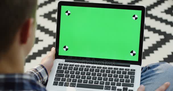 Närbild av vyn över axeln på man sitter med en laptop på sina knän och skriva på den. Grön skärm. Färgtransparens. Spåra rörelse. Mönstrad matta bakgrunden — Stockvideo
