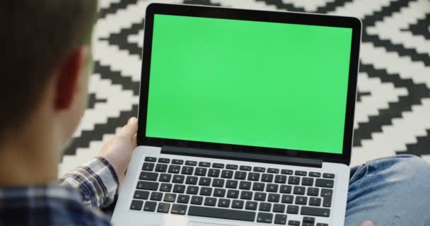 Close up van de weergave over schouder op de man die typt op een laptopcomputer met groen scherm op haar knieën. Chromakey. Patroon floor-achtergrond. — Stockvideo