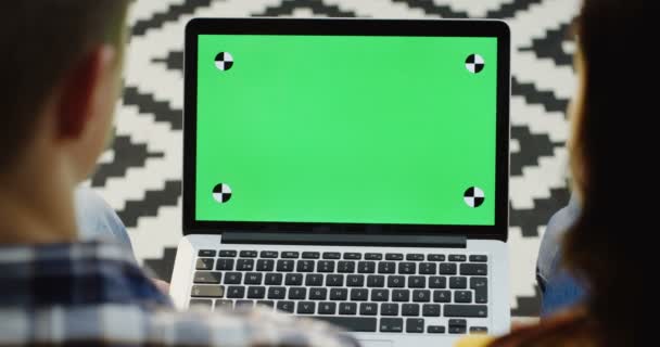 看到一对夫妇坐在膝上的膝上型电脑, 一边看着一些东西。绿色屏幕。色度键。跟踪运动。花纹地板背景 — 图库视频影像