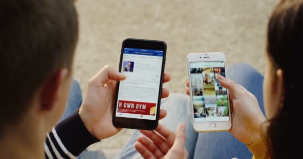 New York - Dec 01, 2017: Over shoulder view on the Caucasian man scrolling facebook app on his black smartphone and woman scrolling Instagram on her white smartphone. Vertically. Close up. Top view — Stock Video