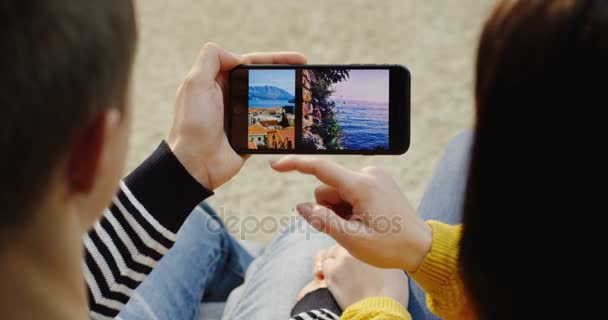 Nueva York - 01 de diciembre de 2017: Vista sobre el hombro de la pareja sentada de la mano, desplazando fotos en el teléfono inteligente negro horizontal y verticalmente. De cerca. Vista superior — Vídeos de Stock