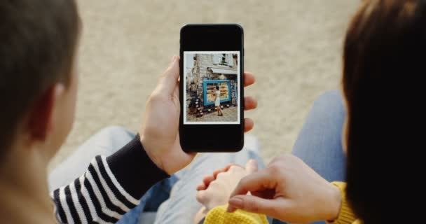 New York - 01 prosinec 2017: přes rameno pohled na pár sedí ruku v ruce, svislé rolování fotografie na černý smartphone a pohledu na sebe. Zblízka. Pohled shora — Stock video