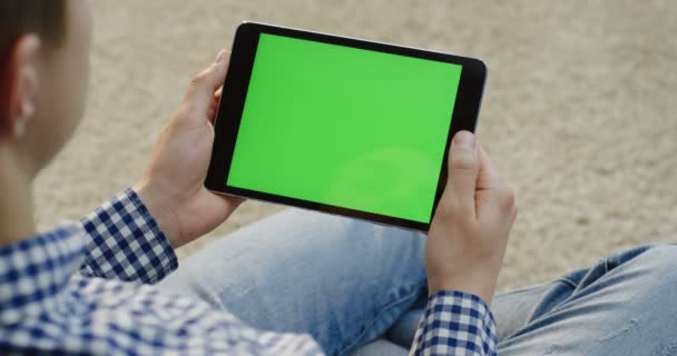 Over de schouder zicht op de blanke man met een zwarte horizontale tablet apparaat zitten en kijken op het. Groen scherm. Chromakey — Stockvideo