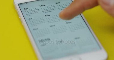 New York - 01 Aralık 2017: En iyi görünümünü parmak kaydırma ve takvim uygulaması sarı masanın üzerinde yatan beyaz smartphone üzerinde taping mans. Yakın çekim