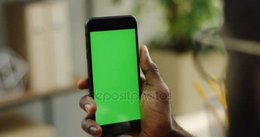 Afro-Amerikan erkek dikey olarak blacksmart telefon tutarak ve üzerinde kaydırma eller. Yeşil ekran. Chroma anahtar. Arka plan bulanık Oda. Yakın çekim