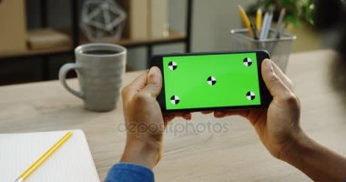 Üstten Görünüm siyah smartphone fincan kahve arka plan ile ahşap Ofis Masası üzerinde yatay olarak holding beyaz erkek eller üzerinde. Yakın çekim. Yeşil ekran. Chroma anahtar. Hareket izleme