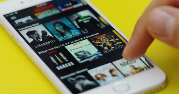 New York - Dec 01, 2017: Närbild av det manliga fingret öppna Netflix app och rulla i den på den vita smartphone som ligger på det gula bordet. — Stockvideo
