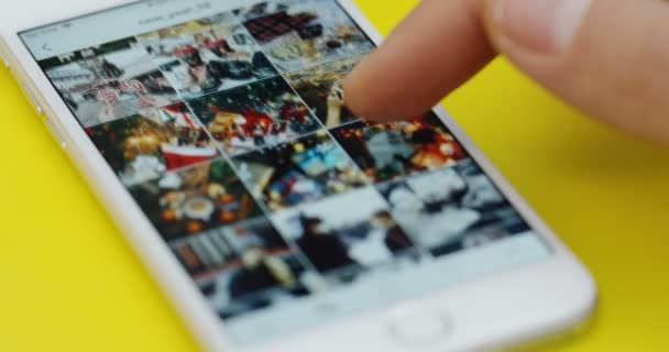 New York - Dec 01, 2017: Close-up van de mans vinger schuiven op de Instagram-app op de witte smartphone liggend op de gele tafel. — Stockvideo