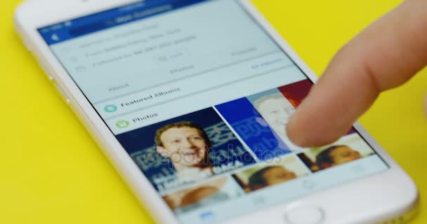 Nueva York - 01 de diciembre de 2017: Acercamiento del desplazamiento del dedo masculino en la aplicación de Facebook en el teléfono inteligente blanco acostado en la mesa amarilla . — Vídeos de Stock