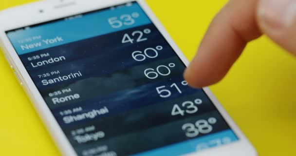 New York - 01. 12. 2017: Pohled shora na mužský prst na předpověď počasí na bílém smartphonu ležícím na žlutém stole. Zavřít — Stock video