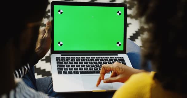 Pareja afroamericana desplazándose en la computadora portátil con pantalla verde y movimiento de seguimiento. Sobre el hombro. Clave de croma. Alfombra estampada — Vídeos de Stock