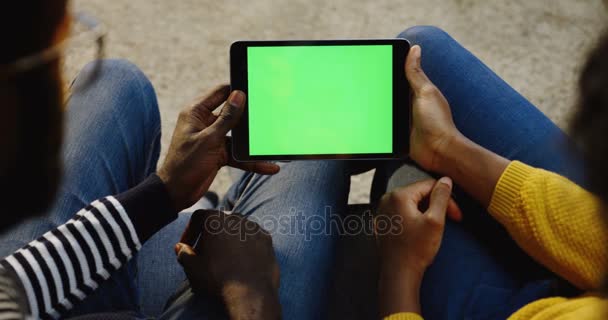 Casal afro-americano segurando um dispositivo tablet preto com tela verde horizontalmente e mulher rolando e gravando nele. Chave Chroma. Por cima do ombro. Fechar — Vídeo de Stock