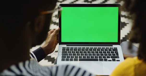 Afro-americano mulher e homem assistindo algo no computador portátil com tela verde na frente deles. Por cima do ombro. Chave Chroma. Tapete modelado — Vídeo de Stock