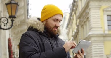 Beyaz delikanlı şapkalı kaydırma ve sokakta onun tablet bilgisayarda soğuk kış gününde kaydediyor. Açık.