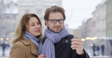 Portre bir kadeh iyi görünümlü orta yaşlı kadın ve kış gününde kar yağıyor ise kare güzel şehirde Smartphone görüntülü sohbet sahip adam. Dışarıda.