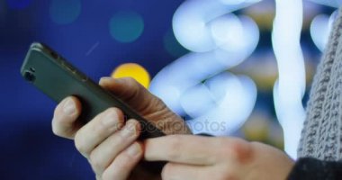İn yakın kaydırma ve bulanık Noel ışıkları arka plan üzerinde siyah Smartphone akşam taping eller mans. Açık havada