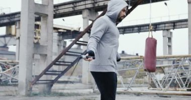 Sisli sabahı bitkilerin atılmış alanında ip atlama atlama gri kapüşonlu bir sakallı çekici beyaz adam. Açık havada