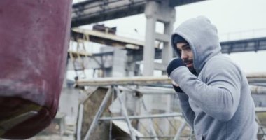 Bir sakallı bir sportif gri eğitim ceket ve başlık kutusunda kırmızı çanta üzerinde egzersiz beyaz çekici adam. Terk edilmiş fabrikası soğuk sisli günde mahveder. Açık havada