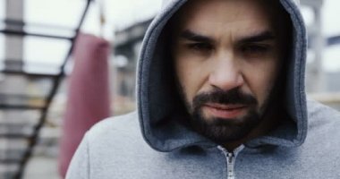 Çekici adamın sakallı ve aşağı ve gözleri kameraya kurnaz bir göz ile yükselen daha seyir gri başlıklı kapatın. Boks kırmızı çanta ve kalıntıları üzerinde arka plan bulanık. Portre