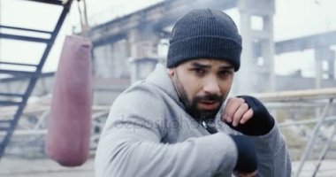 Arka planda bir boks torbası ile eski büyük binalar üzerinde kamera önünde bir kap boksta yakışıklı sporcu mahveder. Soğuk sisli gün. Açık. Yakın çekim. Portre