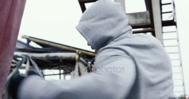 Arka yakın up kötü soğuk gri havada Kırmızı çantalı eğitim boks sahip bir başlık ile yakışıklı adam. Dışarıda büyük bitki kalıntıları.