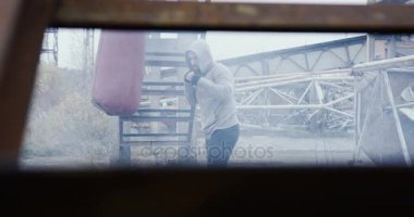 Beyaz adam bir başlık ve bir çanta terk edilmiş eski bitki dışarıda soğuk gri sabah tekme bir sportif giyim.