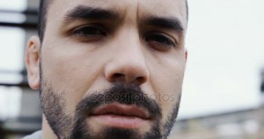 Erkek çekici yüz soğuk gri puslu sabah kamerada ciddi seyir ter damlaları ile kapatın. Arka planda büyük harabeler. Portre. Açık