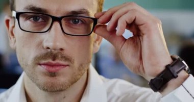 Beyaz çekici genç adam arıyor ve içtenlikle kameraya gülümsemek için başlangıç bardaklarda kapatın. Bulanık ofis alanı arka plan. Portre vurdu. Kapalı