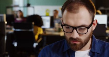 Yakışıklı genç beyaz adamın bulanık office arka plan fotoğraf makinesini düz içine ararken bardaklarda kapatın. Ofis çalışanı portre çekim