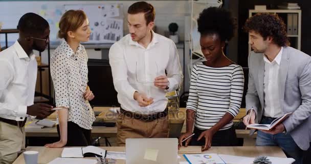 Jovem equipe de negócios multi-étnica trabalhando em um projeto e seu chefe dando-lhes tarefas no aconchegante escritório moderno. Planeando uma startup. Para dentro — Vídeo de Stock