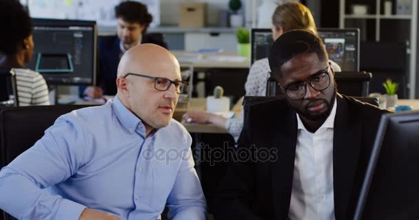 Retrato de jovem trabalhador de escritório afro-americano consultando com seu chefe sobre sua estratégia de projeto de negócios no computador. Escritório urbano com trabalhadores em fundo turvo. Interior — Vídeo de Stock