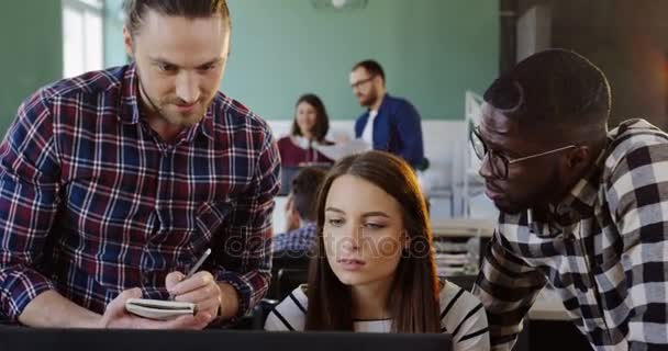 Fiatal férfi és női irodai dolgozók megvitatni egy üzleti projekt a számítógépen. A városi Hivatal barátságos csapat. — Stock videók