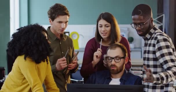 Junges multiethnisches Team von Geschäftsleuten, die sich über ein Geschäftsprojekt unterhalten und darüber diskutieren. Gruppe von Frauen und Männern steht im städtischen Büro und schaut auf den Computer. — Stockvideo