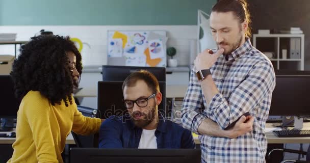 Kaukasiska stilig man i glas som ger råd till African American curly ung kvinna på ett affärsprojekt. Ung kvinna och mannen tittar på boss datorn i moderna office atmosfären. — Stockvideo