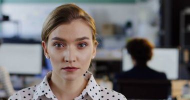 Kafasını kameraya dönüm ve içtenlikle gülümseyen sevimli genç kadın kapatın. Bulanık ofiste işçi bilgisayar arka plan ile. Kapalı. Portre