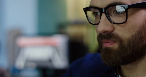 Nahaufnahme eines gutaussehenden jungen kaukasischen Mannes mit Brille, der spät am Computer arbeitet. der verschwommene Hintergrund. Innenraum. Porträt — Stockfoto