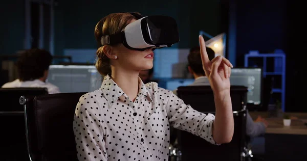 Young female office worker having a VR headset at her workplace in the evening. VR glasses. Inside the big office room