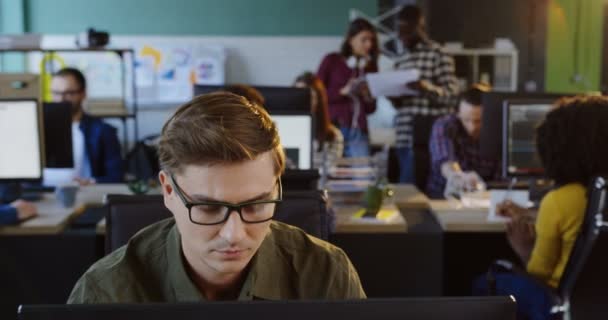 Portrait de jeune homme caucasien séduisant en lunettes travaillant sur ordinateur et dans l'espace de bureau urbain. Des employés de bureau sur fond flou. Gros plan .