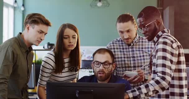 Jonge vriendelijke multi-etnische kantoorpersoneel maken van een strategie voor een project opstarten op de computer. Office-team van de mannen en vrouw in de comfortabele, mooie kantoorruimte. — Stockvideo