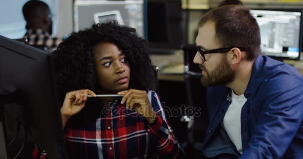 Női afro-amerikai, és a férfi kaukázusi munkatársai megvitatni a projekt sturtup este irodában. Emberek a számítógépek a háttérben. — Stock videók